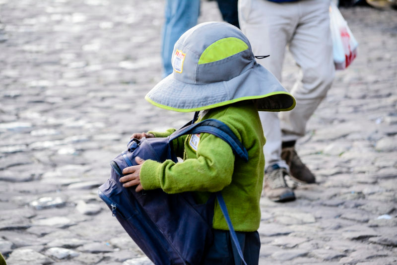 A small child seen from behind, wearing a blue backpack, walking alone along a street.
