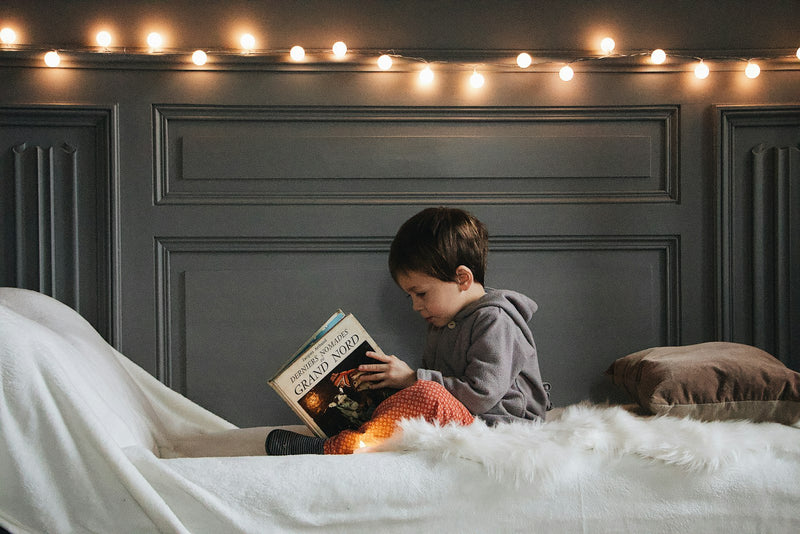 A young boy reading a book in bed at bedtime