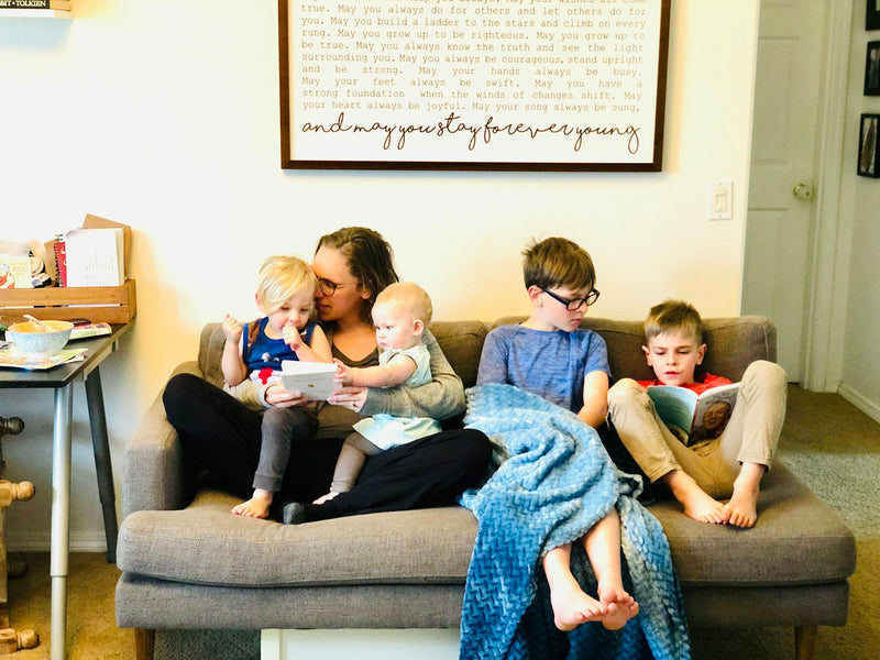 Three children sitting together on a couch reading in a bright living room