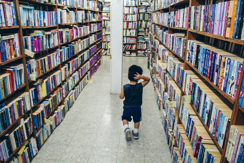 A boy stands in front of a bookshelf, looking at the books in front of him.