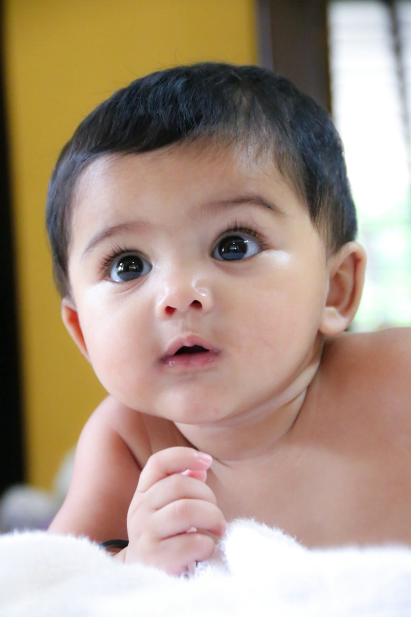 A baby with wide, curious eyes looking upward in wonder, photographed in Udupi, India