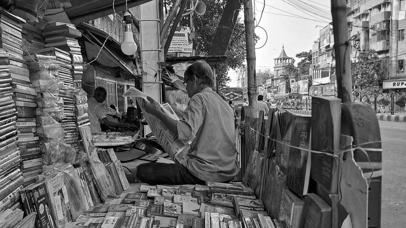 A street bookseller sitting among piles of books in the back of a truck on a street in Kolkata, India