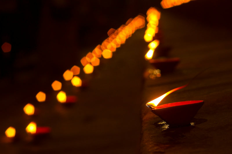 Rows of lit oil lamps glowing along a riverside ghat at dusk.