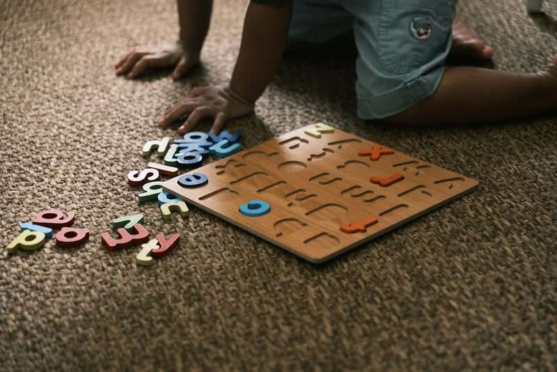 A young child playing with a wooden alphabet puzzle on the carpet