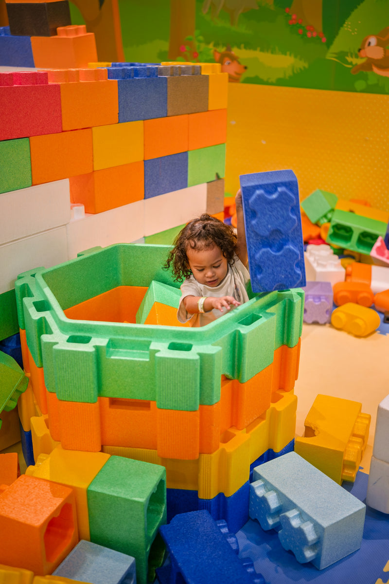 A child plays with large, colorful building blocks on the floor.