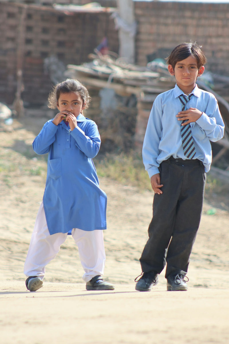 Two young South Asian children in blue school uniforms outdoors on a school day