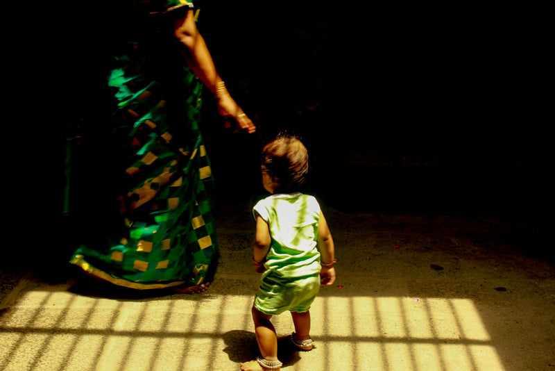 A woman in a green sari sits with a child in a sunlit room at home.