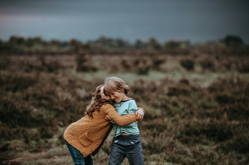 Two young children hugging each other outdoors in front of an open field.