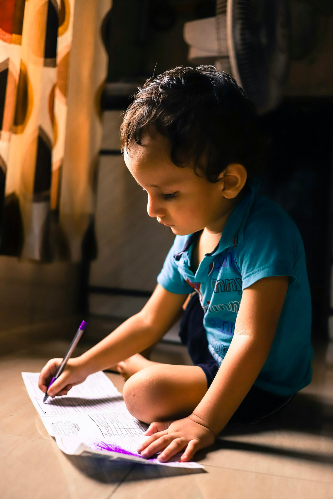 A young boy sitting near a sunlit window, concentrating while writing on white paper