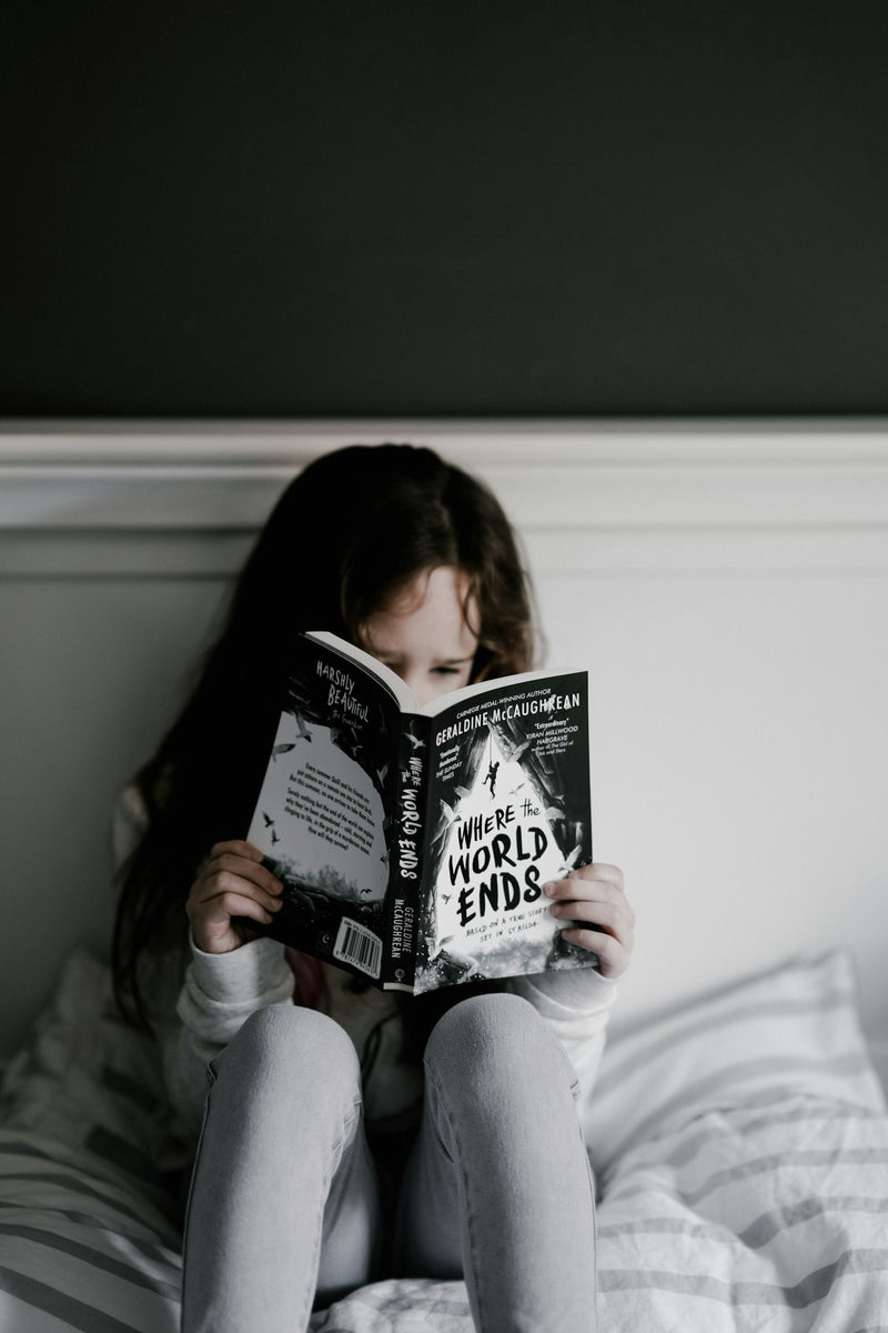 A child reading a book while sitting on a bed