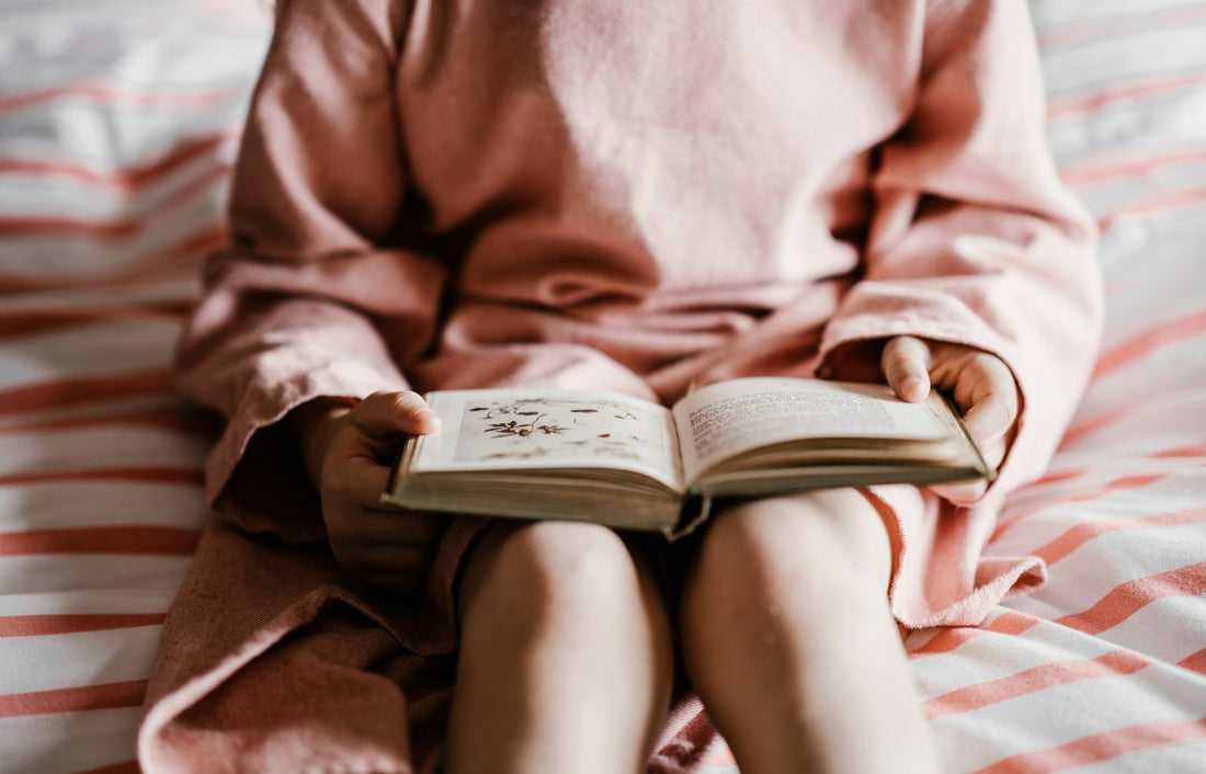 A child reading on a bed covered with a red and white striped bedspread