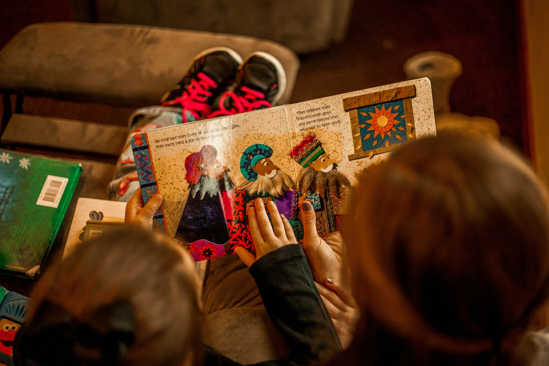 Two young children sitting together on a sofa, engaged with an open picture book