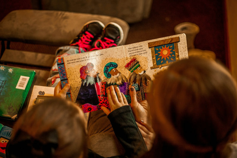 Two young children sitting together on a sofa, engaged with an open picture book