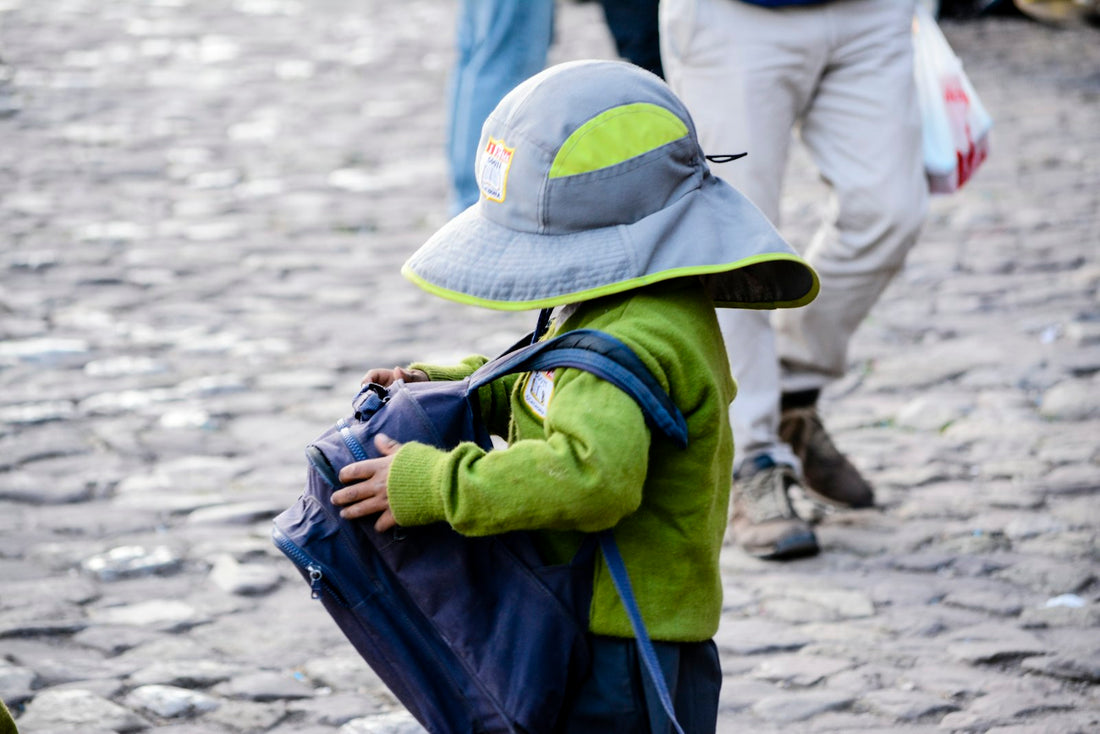 A small child seen from behind, wearing a blue backpack, walking alone along a street.