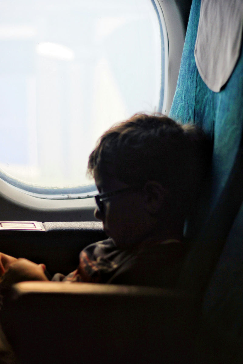 A toddler sits in an airplane seat near a window.