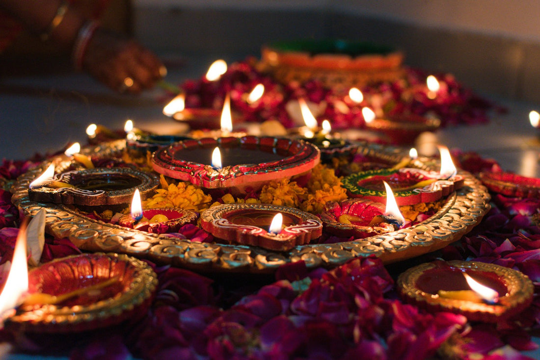Lit clay diyas arranged on a decorative tray surrounded by scattered flower petals for Diwali