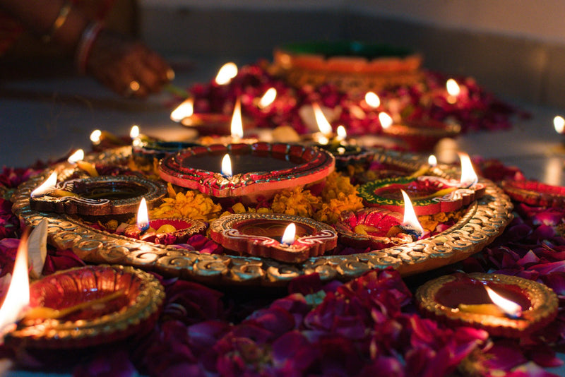 Lit clay diyas arranged on a decorative tray surrounded by scattered flower petals for Diwali