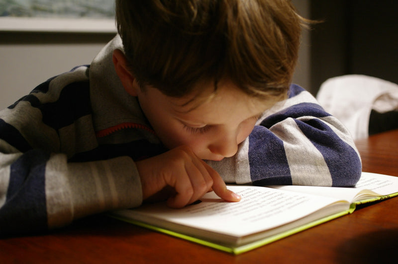 A young child in a striped shirt reading a book at a wooden table