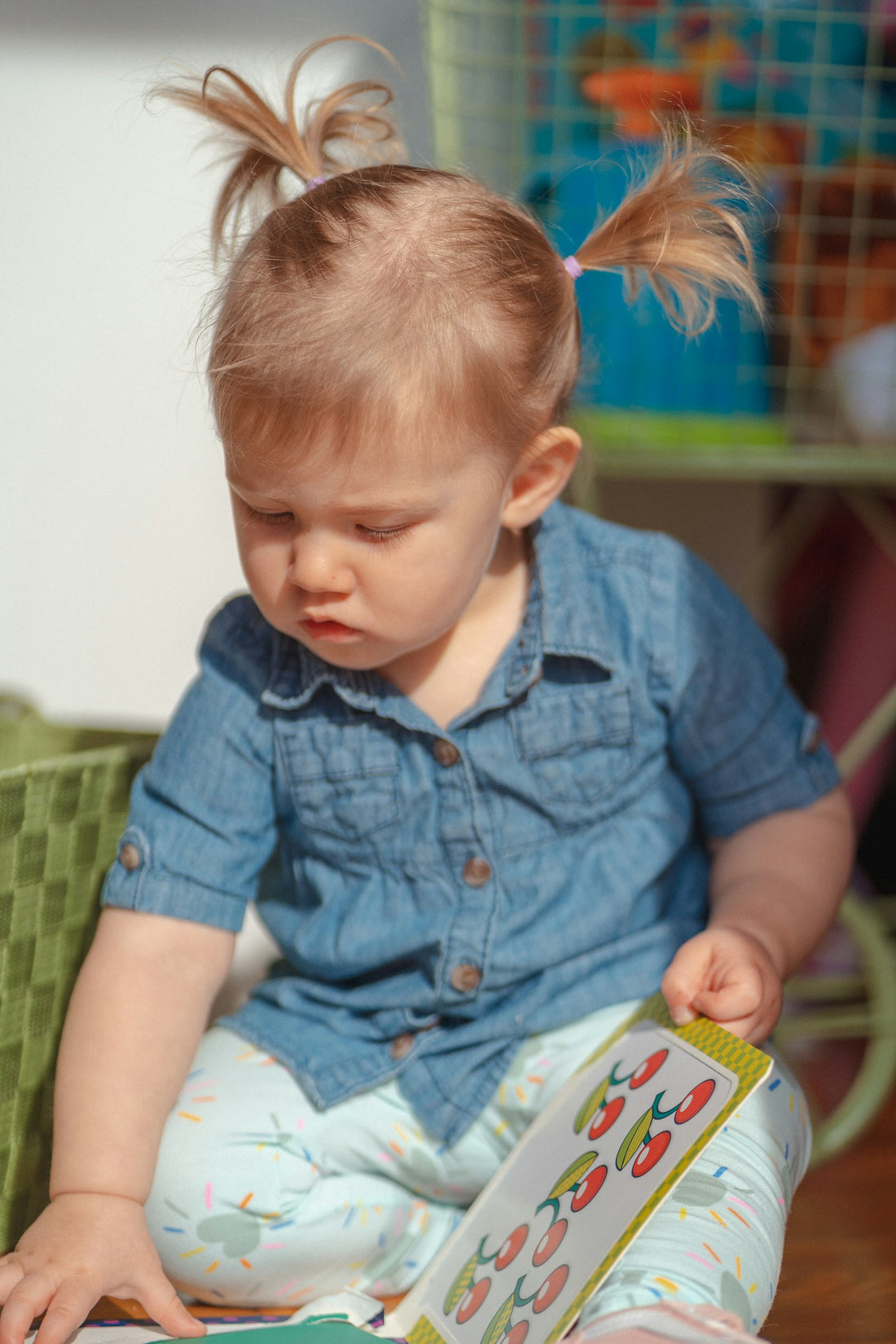 A young girl in denim clothing sitting on the floor, engrossed in reading a book.