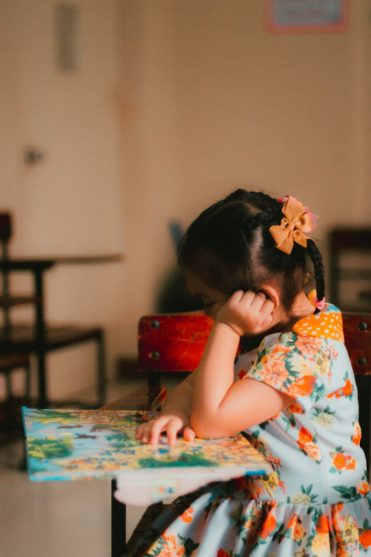 A young girl sitting at a table, reading from an open book.