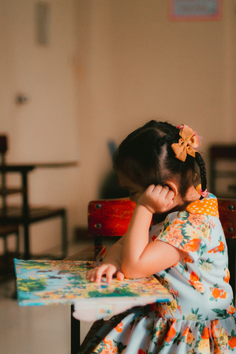 A young girl sitting at a table, reading from an open book.