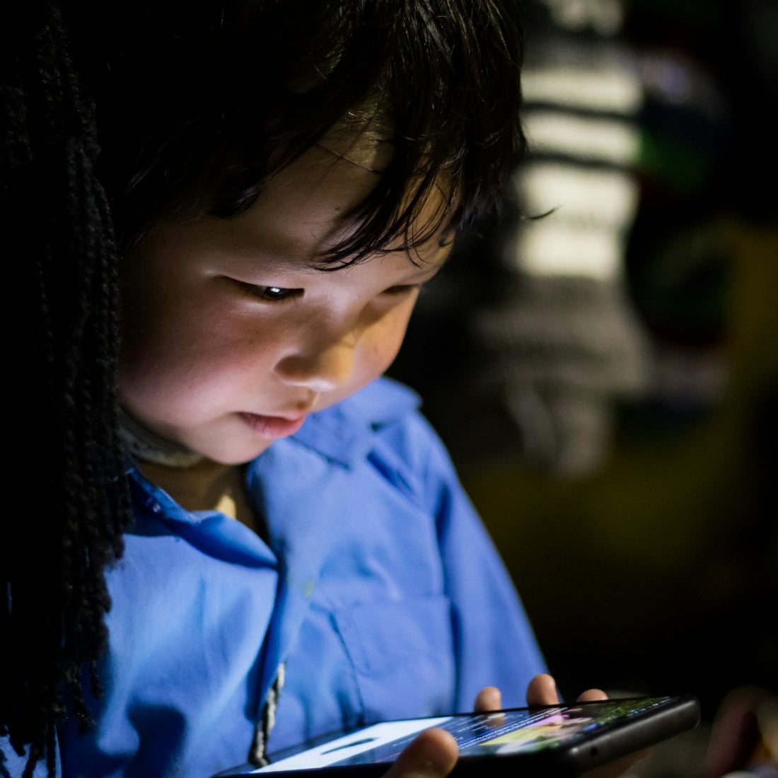 A young child outdoors in Dharamshala gazing intently at a tablet screen