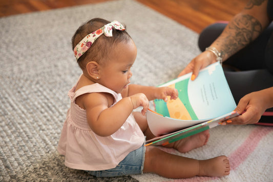 A toddler sitting indoors, absorbed in an open picture book.