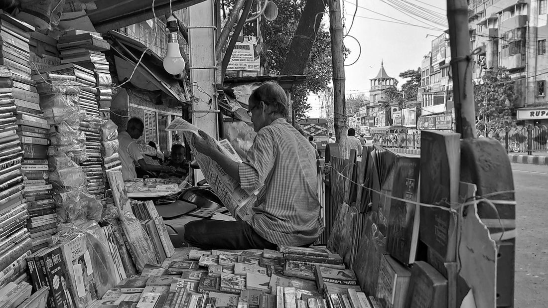 A street bookseller sitting among piles of books in the back of a truck on a street in Kolkata, India