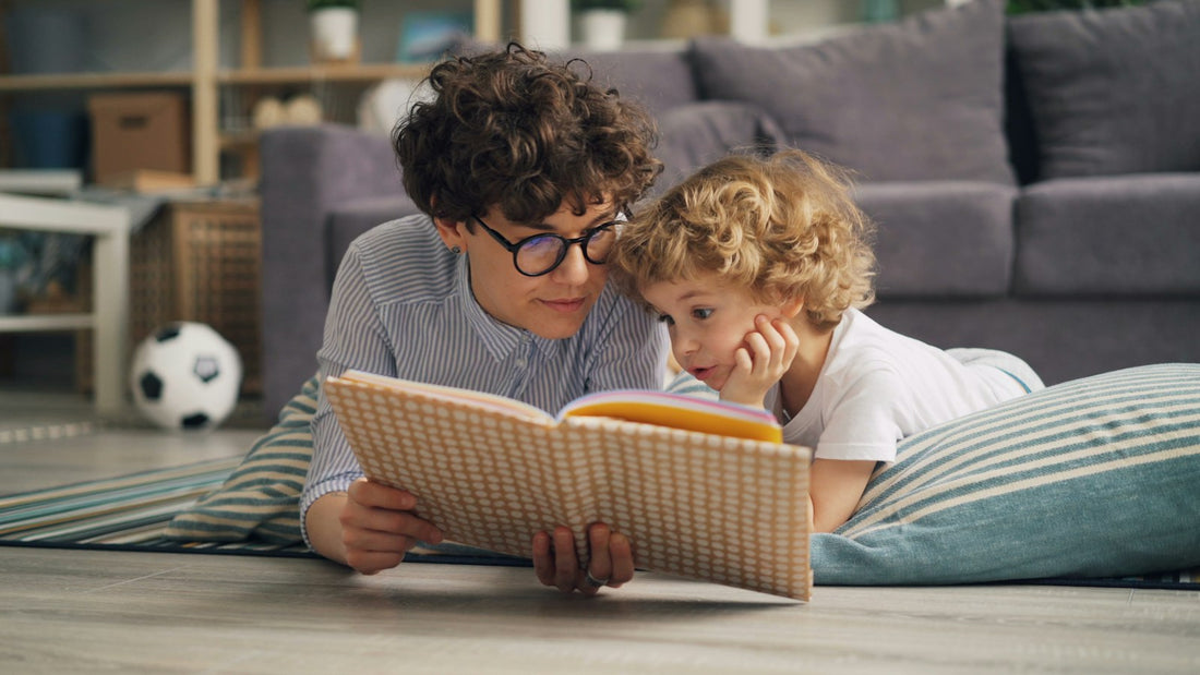 A parent and child lying on the floor together, reading a book.