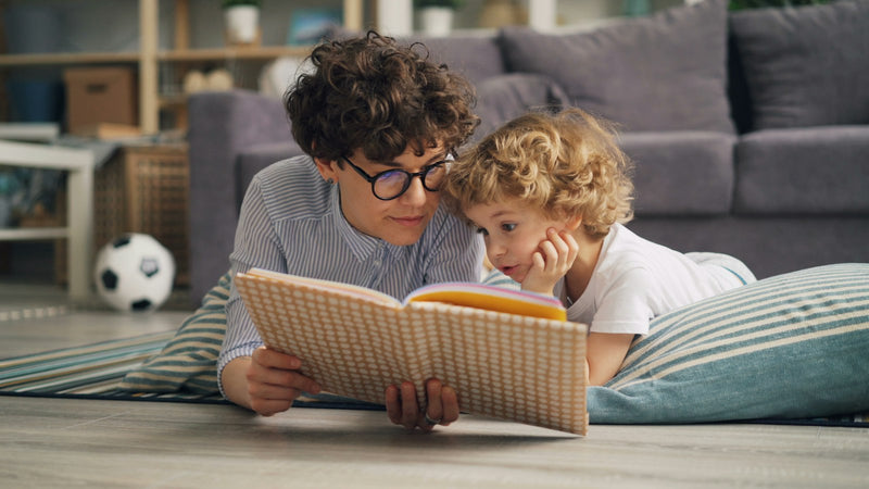A parent and child lying on the floor together, reading a book.
