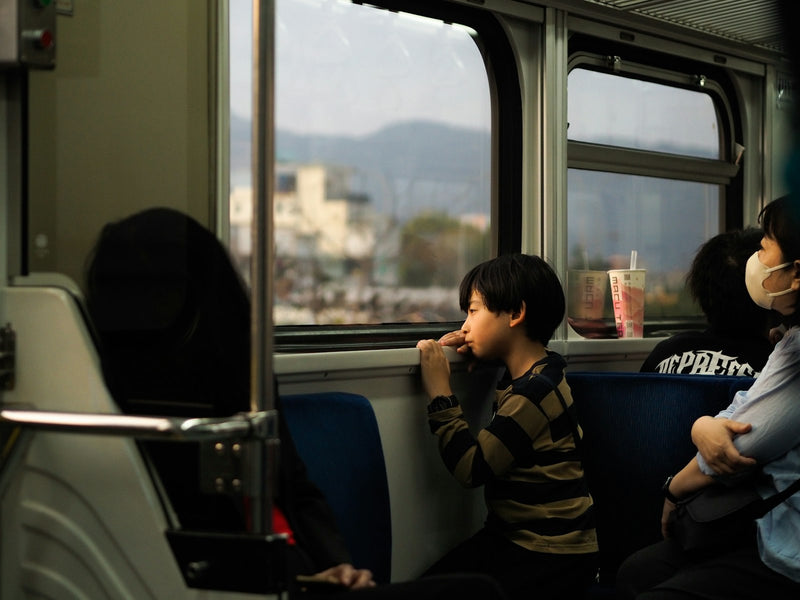 A young boy gazing thoughtfully out of a train window, lost in thought