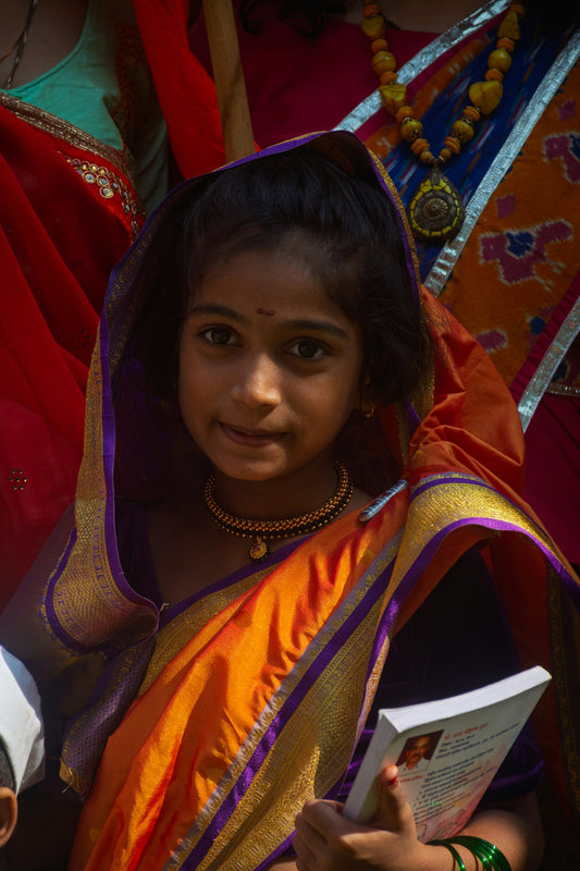 A young girl in traditional Indian attire with a green sari and bangles, indoors, holding an open book